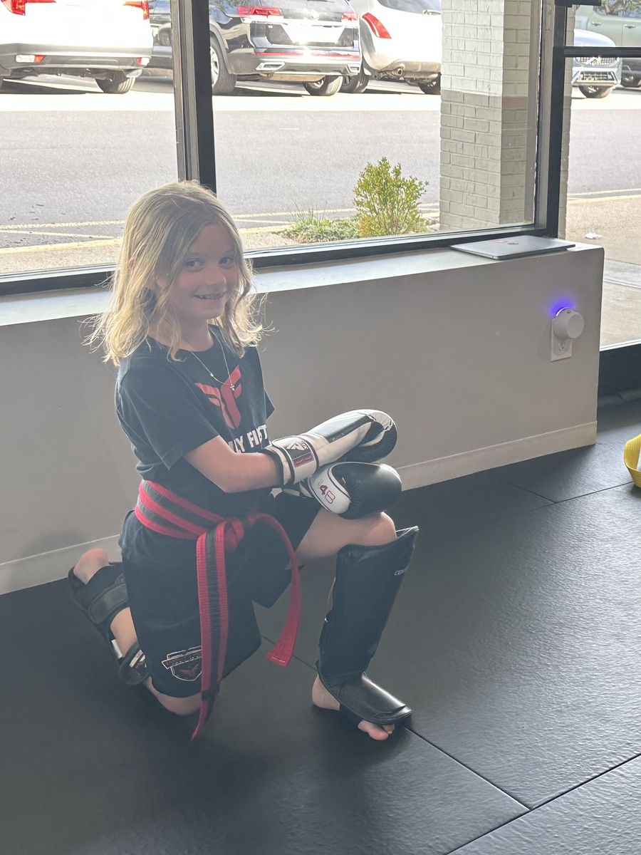 A Tiny Titans student smiling in boxing gloves at Family First Martial Arts in Franklin