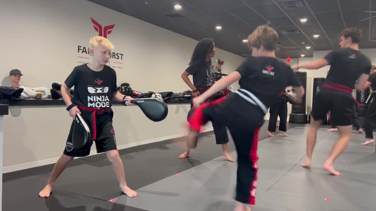 Students drilling kicks on pads in front of the Family First logo wall in Franklin, TN