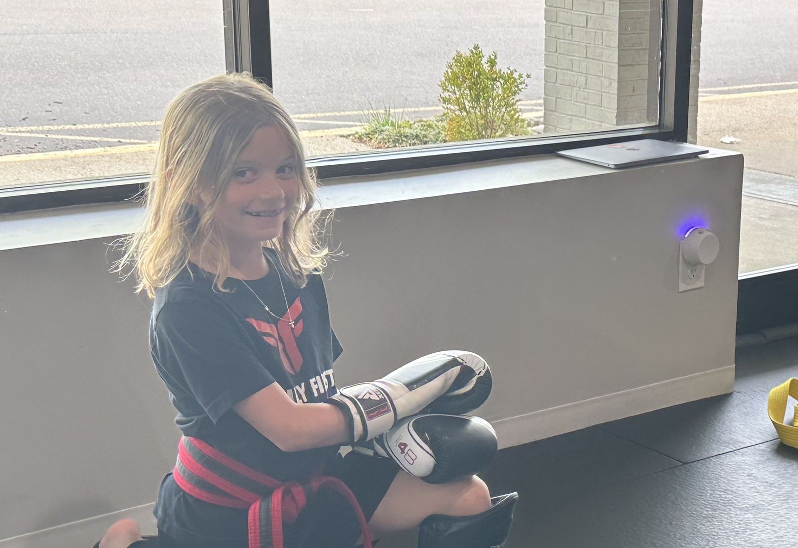 A smiling Tiny Titans student in boxing gloves at Family First Martial Arts Franklin